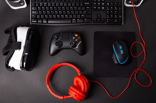 Photo of gaming gear, mouse, keyboard, joystick, headset on black table background.